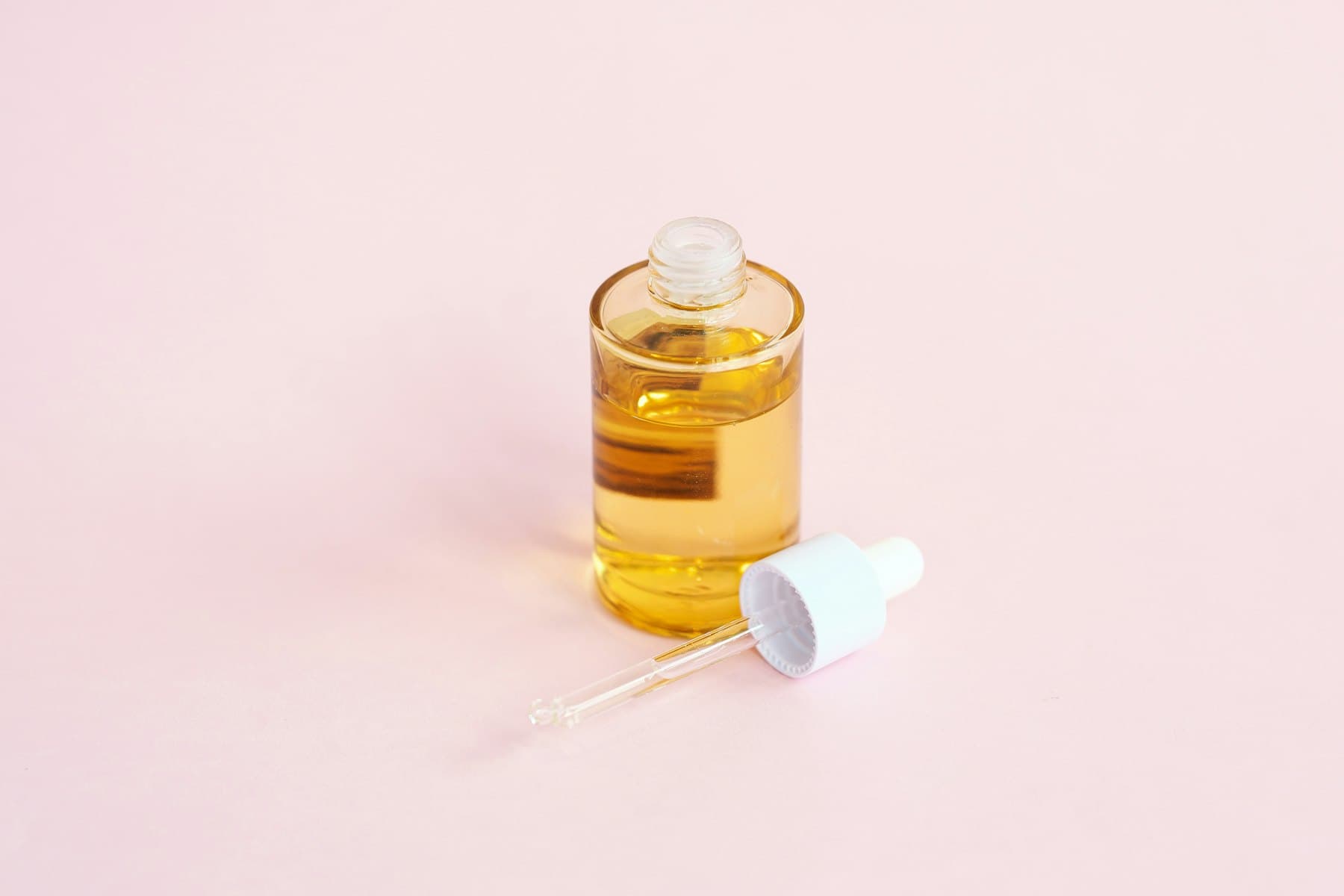 Frasco de sérum con gotero sobre una superficie rosa